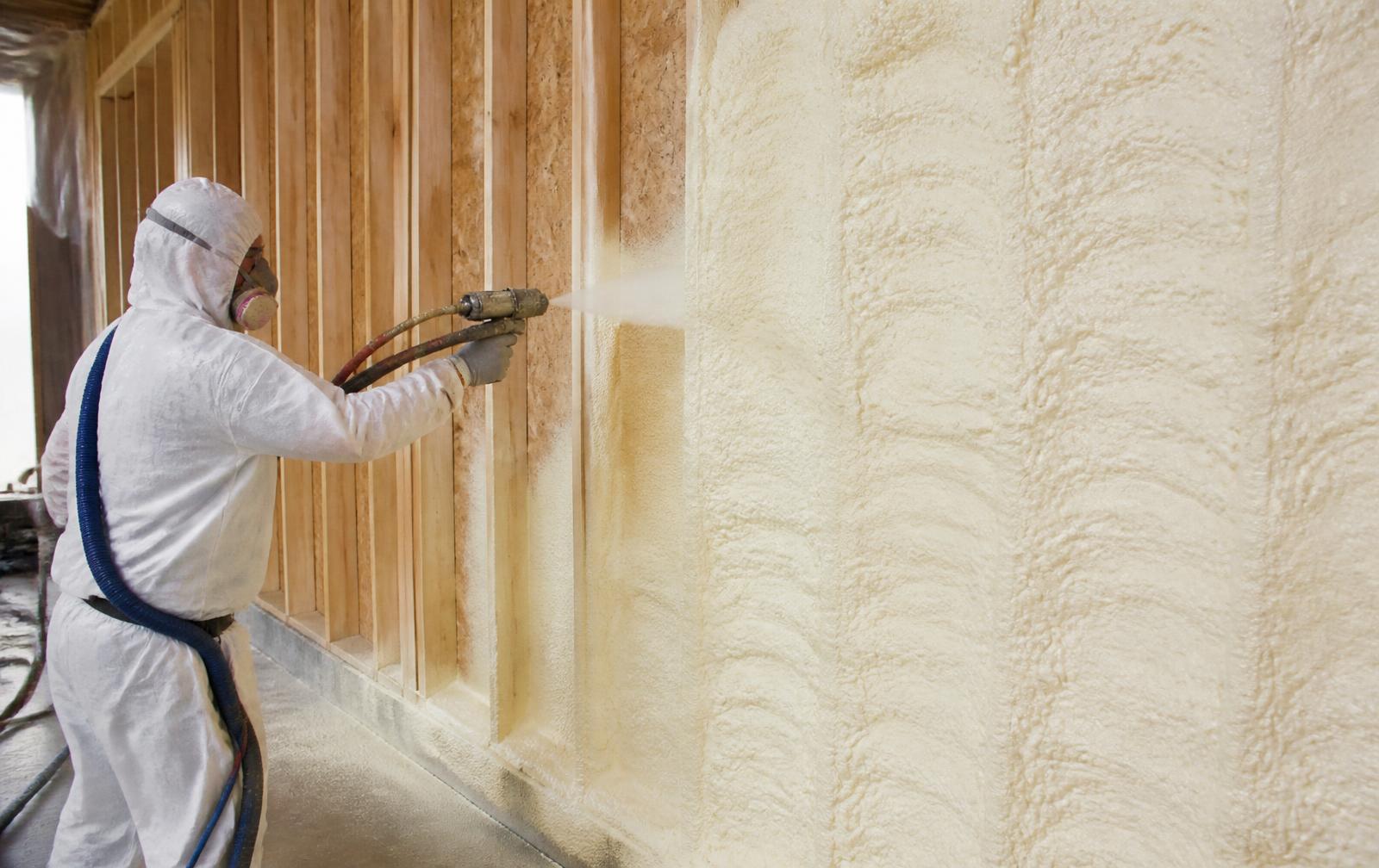 Worker applying sprayed polyurethane foam insulation to a building wall